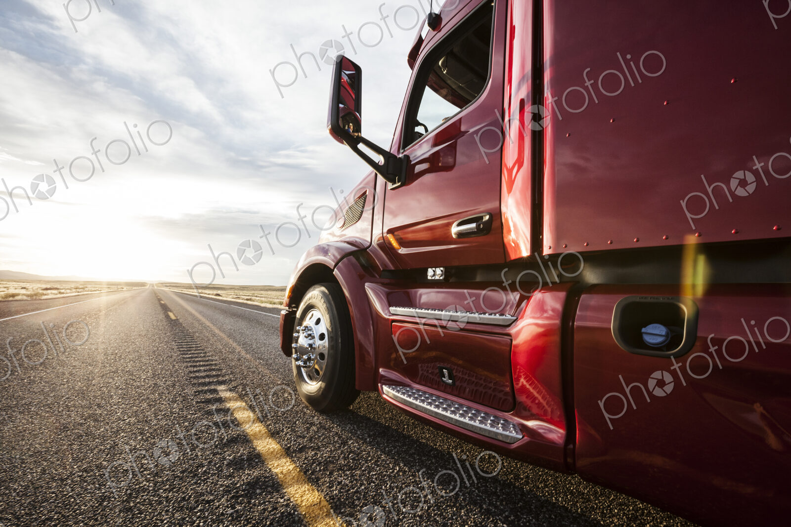 Close up side view looking forward of a commercial truck on a highway at sunset.