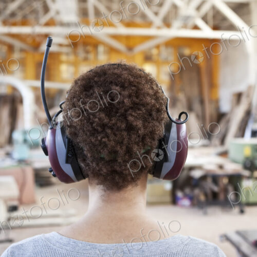 Close up view from behind of a woman factory worker wearing hearing protection in a…