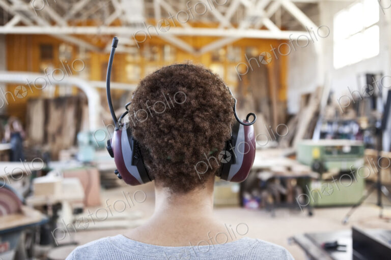 Close up view from behind of a woman factory worker wearing hearing protection in a…