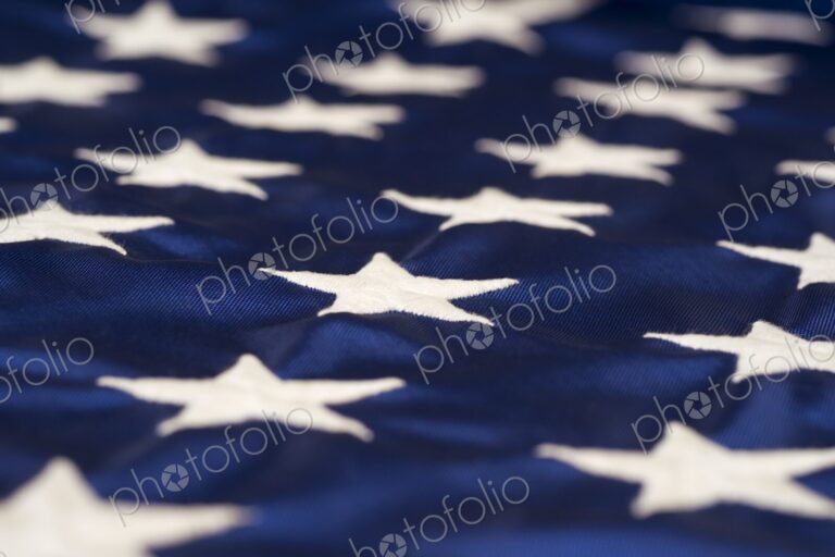 Close-up view of white embroidered stars on the blue field of the American flag -…