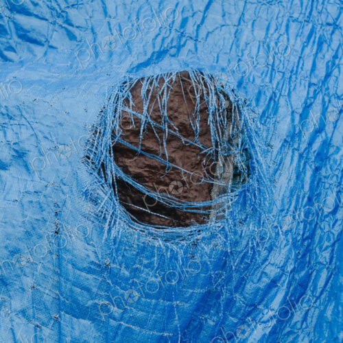 Close up worn blue tarp with tattered hole in center