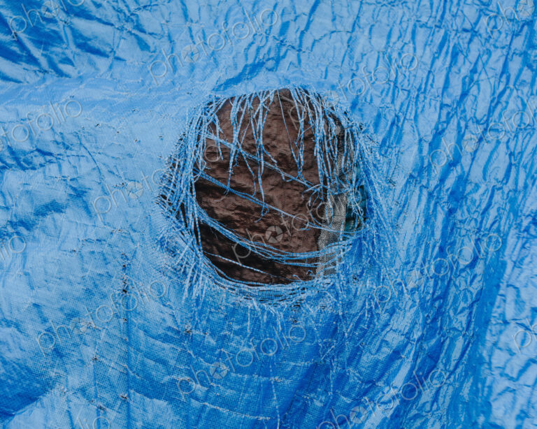 Close up worn blue tarp with tattered hole in center