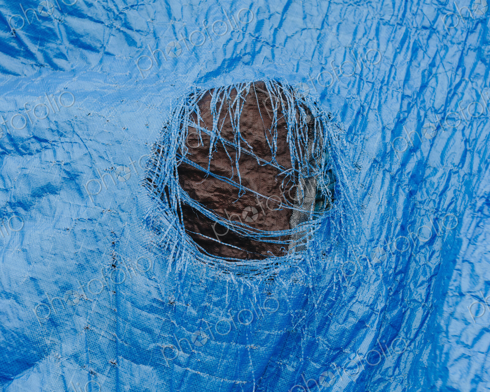 Close up worn blue tarp with tattered hole in center