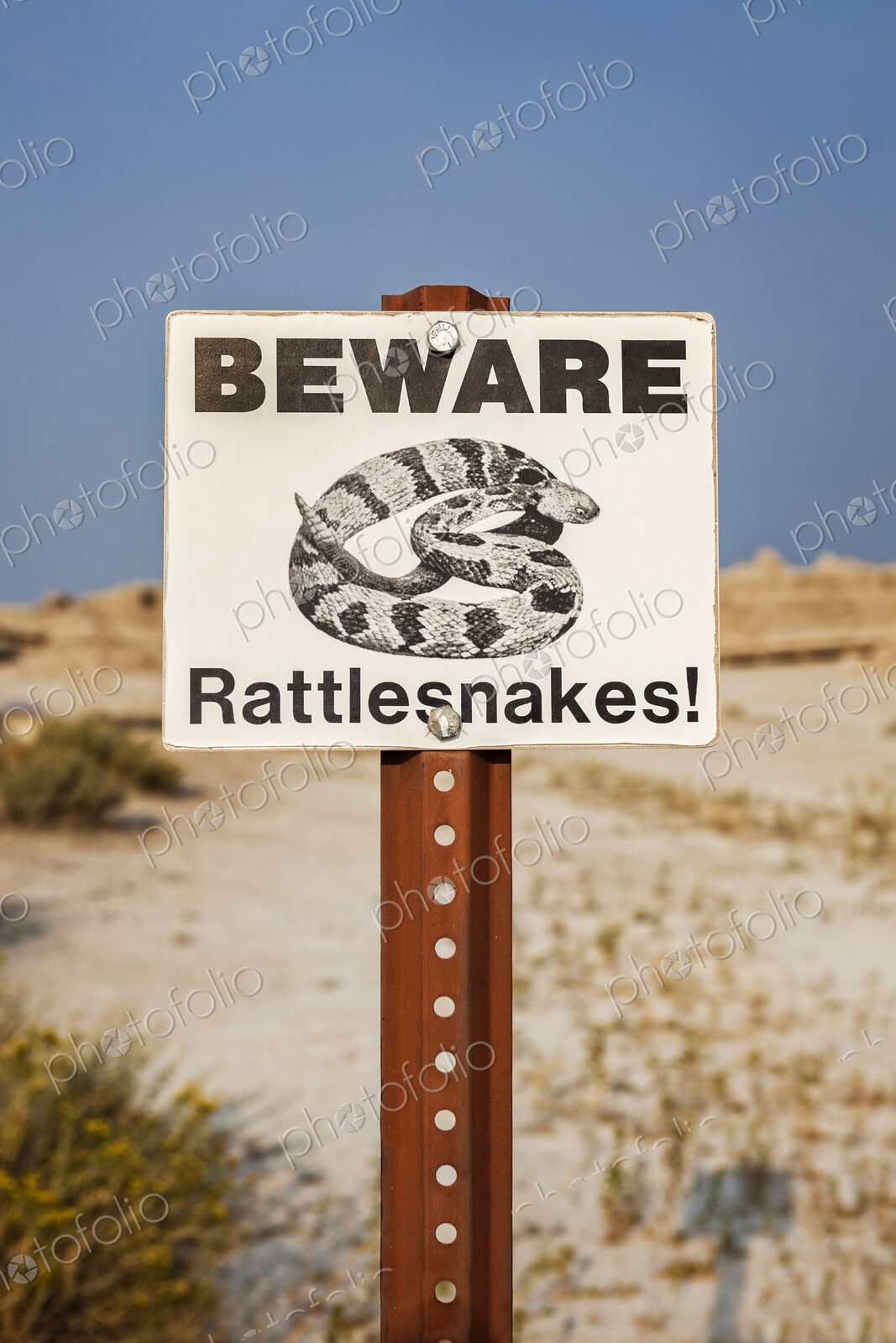Close view of a Beware Rattlesnakes sign against blue sky and dry prairie in Badlands…