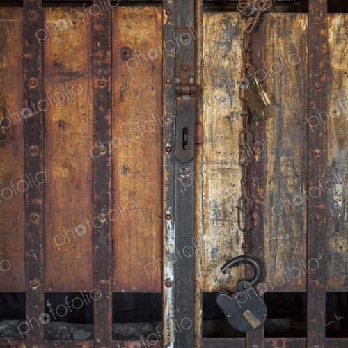 Close view of a frontier jail door with rusty iron bars, chain, and padlock against…