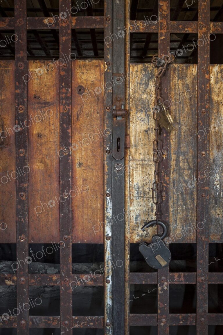 Close view of a frontier jail door with rusty iron bars, chain, and padlock against…