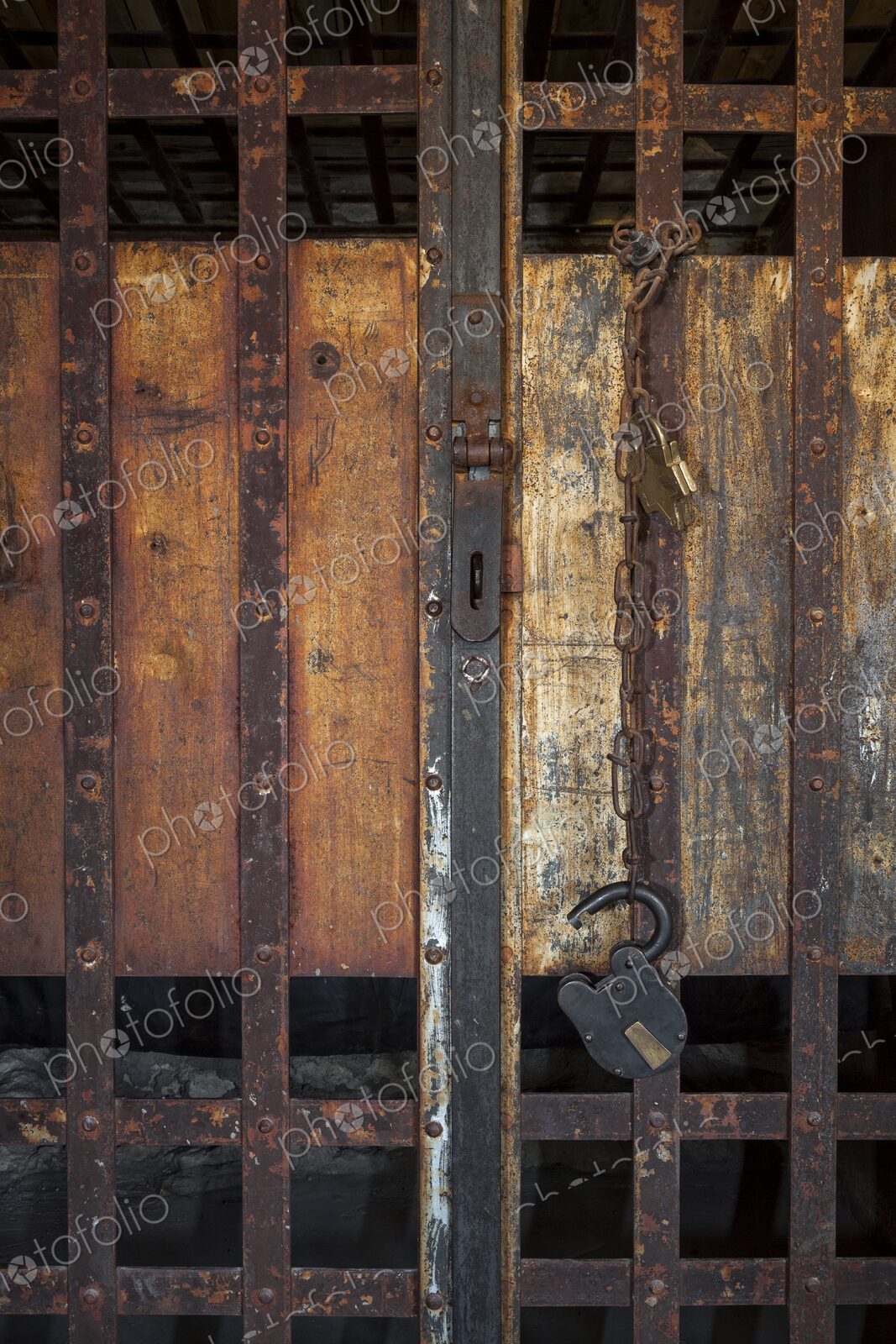 Close view of a frontier jail door with rusty iron bars, chain, and padlock against…