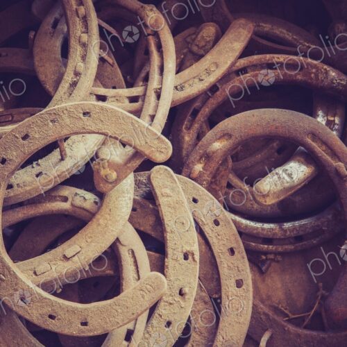 Close view of a pile of old rusty horseshoes in a barn, showing weathered metal,… Close view of a pile of old rusty horseshoes in a barn, showing weathered metal,…