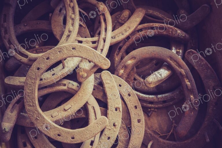 Close view of a pile of old rusty horseshoes in a barn, showing weathered metal,…