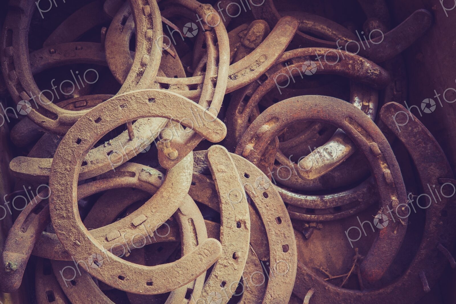 Close view of a pile of old rusty horseshoes in a barn, showing weathered metal,…