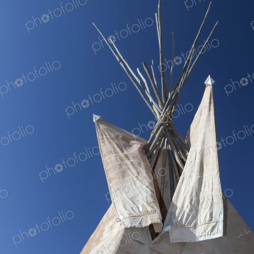 Close view of a traditional Plains tipi with canvas flaps and wooden poles reaching…