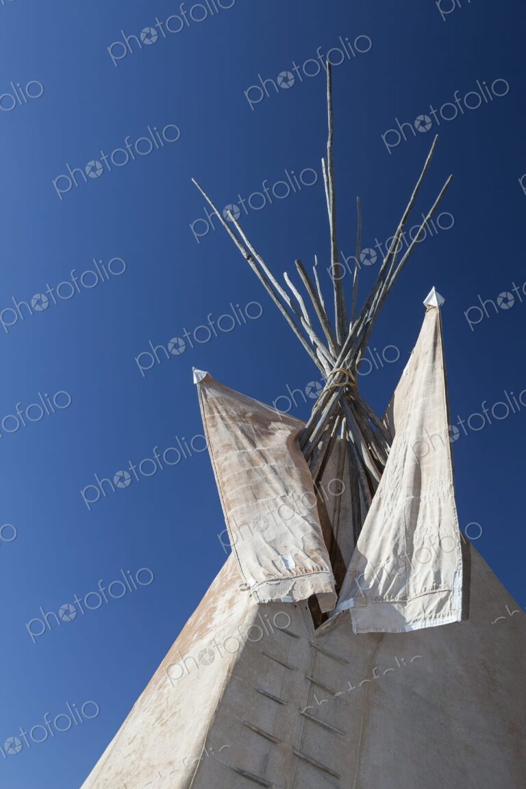 Close view of a traditional Plains tipi with canvas flaps and wooden poles reaching…