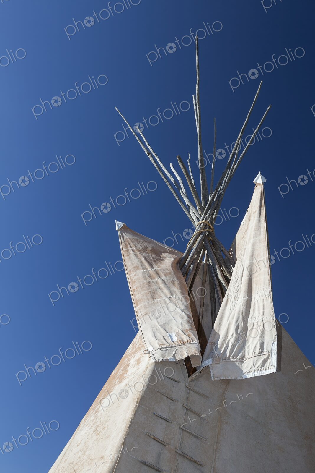 Close view of a traditional Plains tipi with canvas flaps and wooden poles reaching…