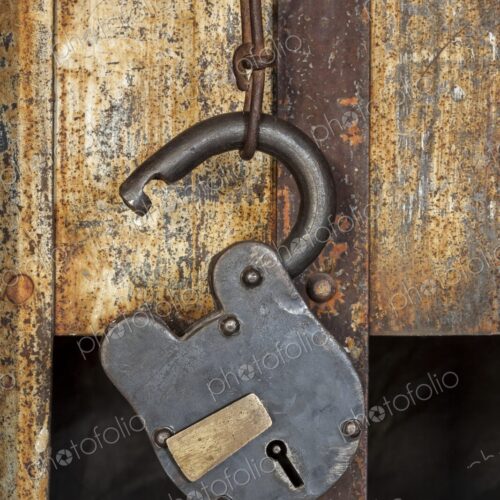 Close view of a vintage padlock and chain hanging on a rusty jail door, with iron bars… Close view of a vintage padlock and chain hanging on a rusty jail door, with iron bars…