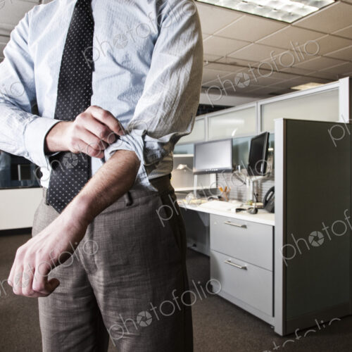 Closeup of a Caucasian businessman wearing a dress shirt and tie and rolling up his… Closeup of a Caucasian businessman wearing a dress shirt and tie and rolling up his…