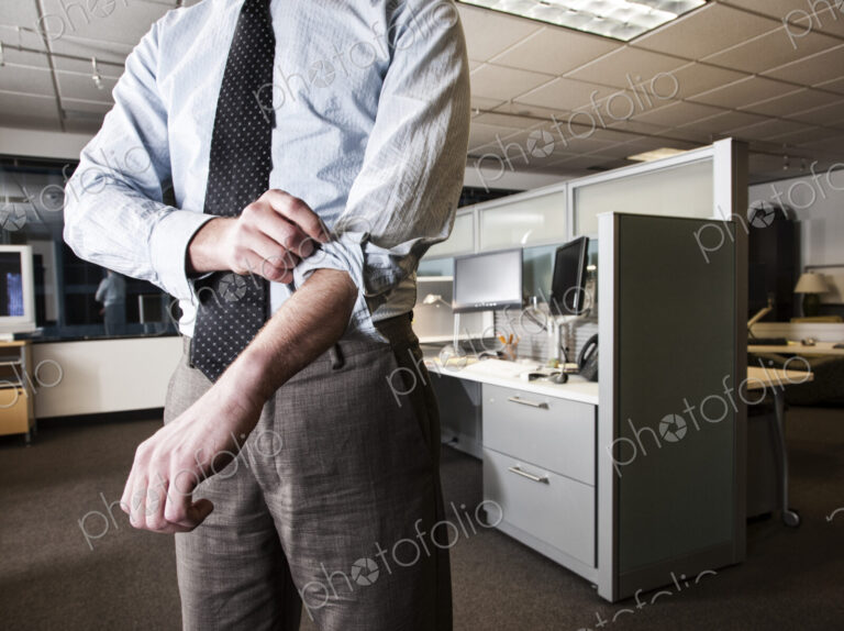 Closeup of a Caucasian businessman wearing a dress shirt and tie and rolling up his…