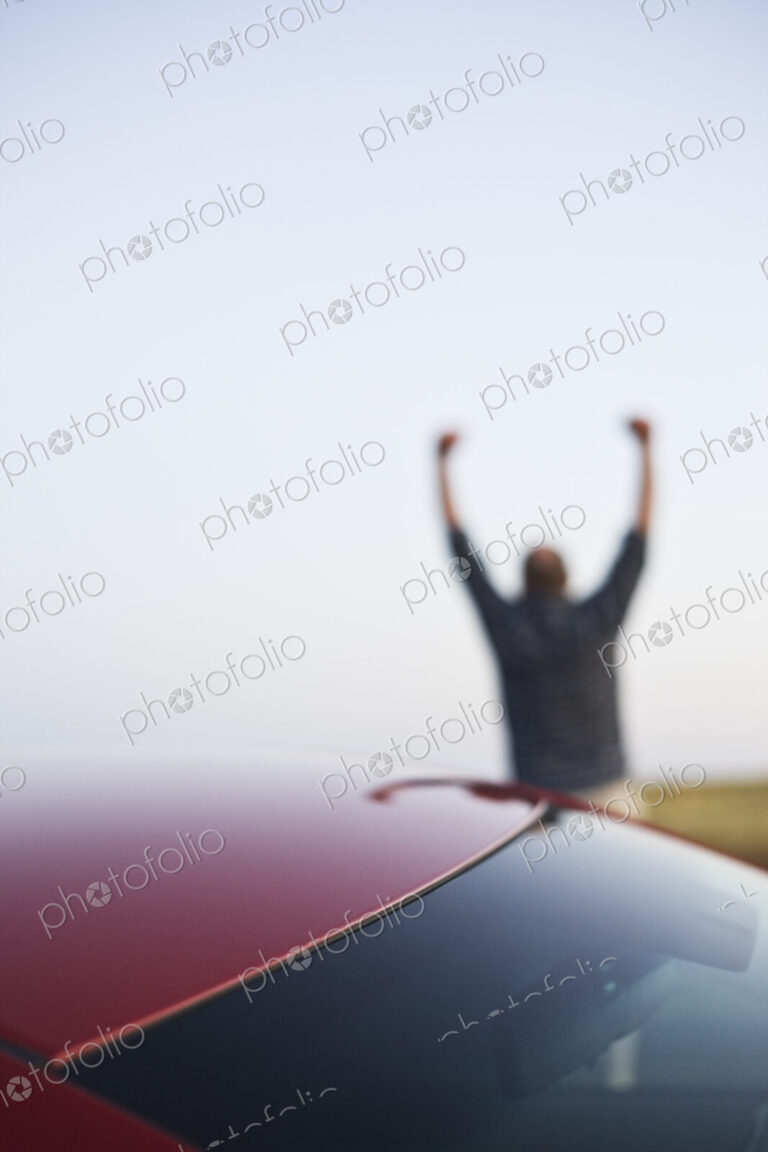Closeup of a car window and a single male celebrating with his arms up in the background.