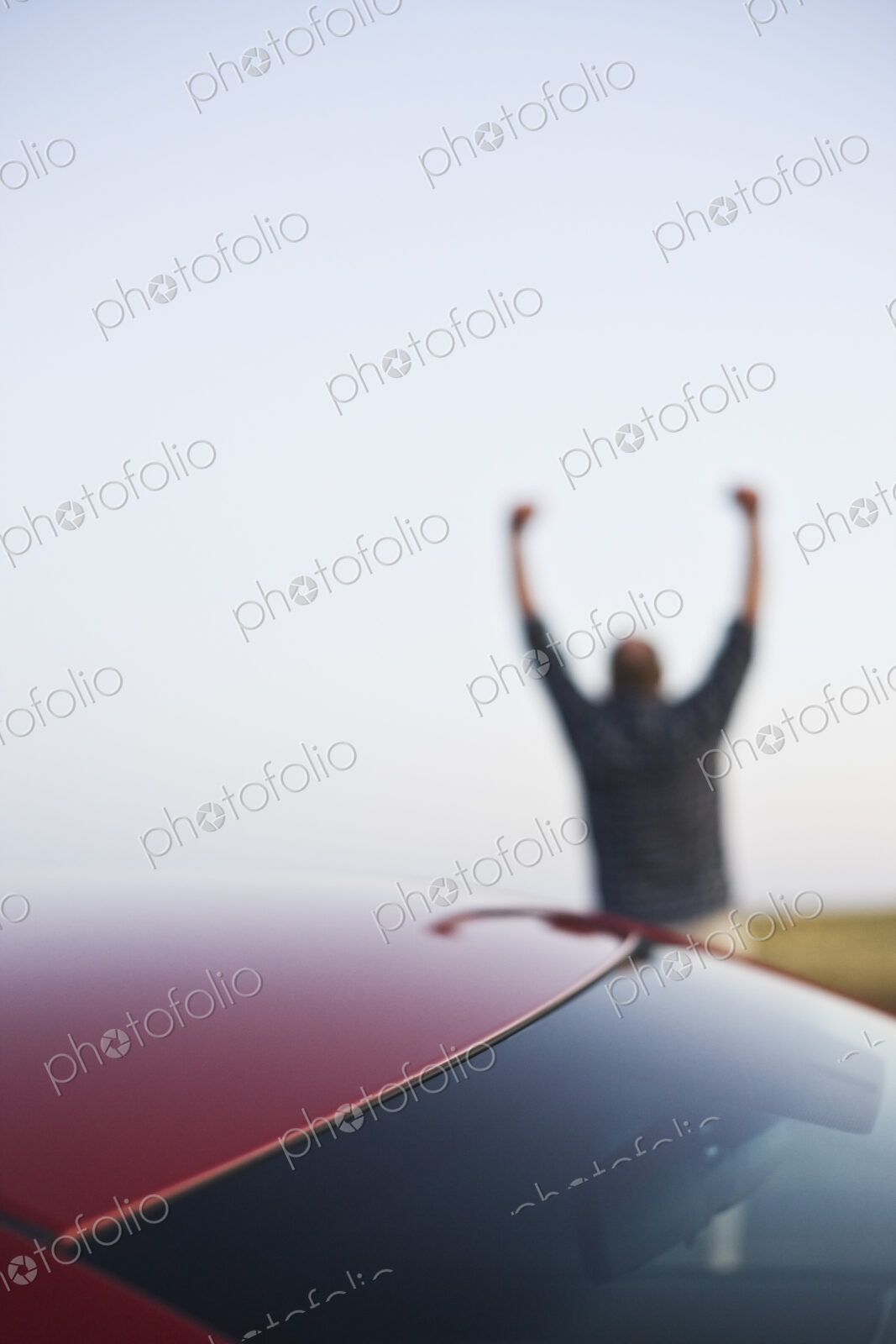 Closeup of a car window and a single male celebrating with his arms up in the background.