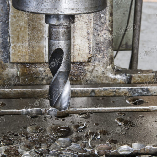 Closeup of a drill bit in a drill press in a sheet metal factory.