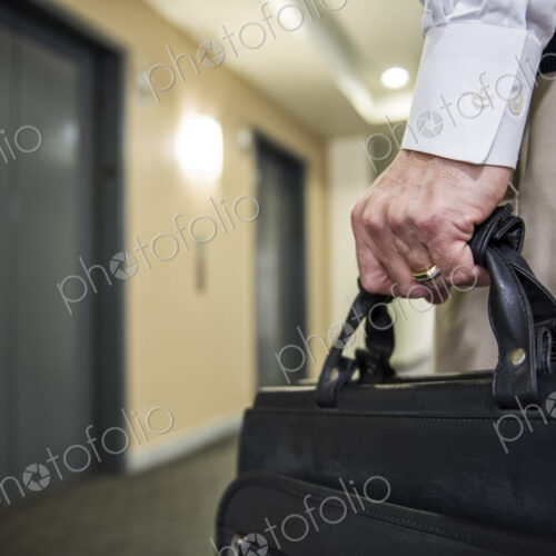 Closeup of a hand carrying a brief case in an office environment.