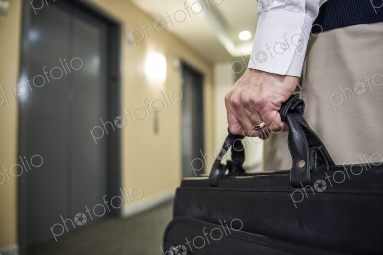 Closeup of a hand carrying a brief case in an office environment.