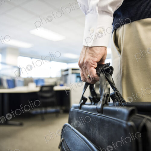 Closeup of a hand carrying a brief case in an office environment.
