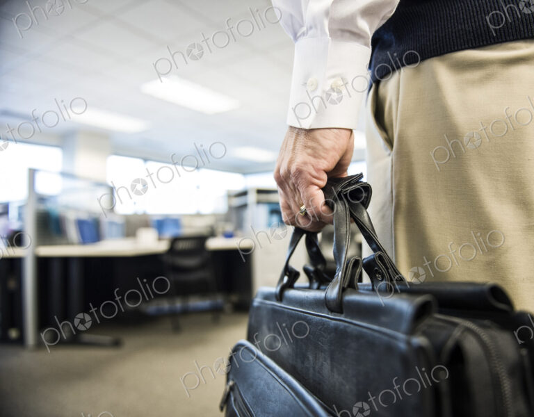 Closeup of a hand carrying a brief case in an office environment.