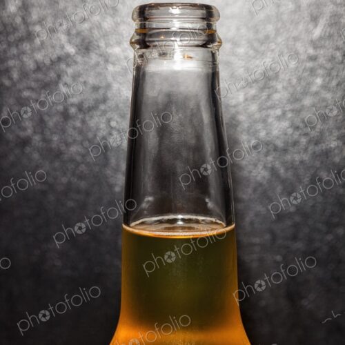 Closeup of clear glass beer bottle with cold beer against a black leather background Closeup of clear glass beer bottle with cold beer against a black leather background