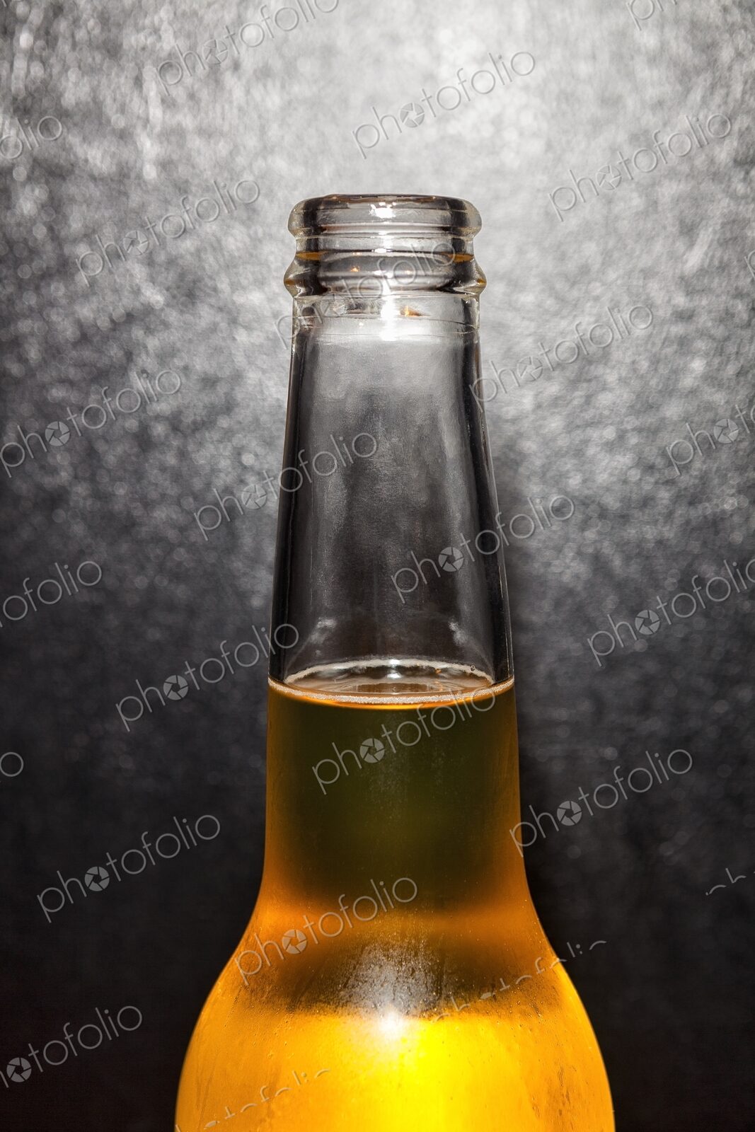 Closeup of clear glass beer bottle with cold beer against a black leather background