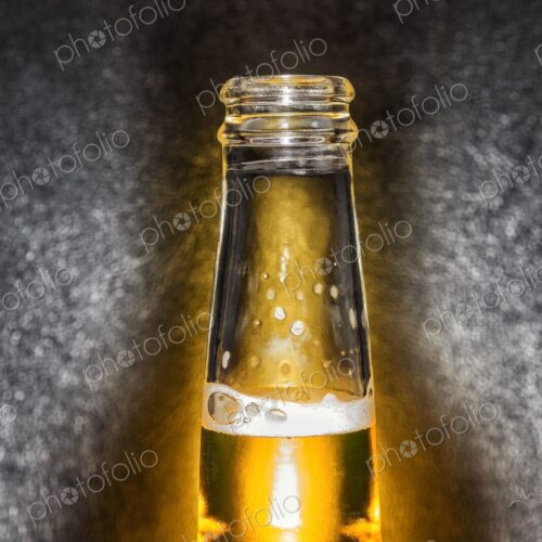 Closeup of clear glass beer bottle with cold beer against a black leather background Closeup of clear glass beer bottle with cold beer against a black leather background