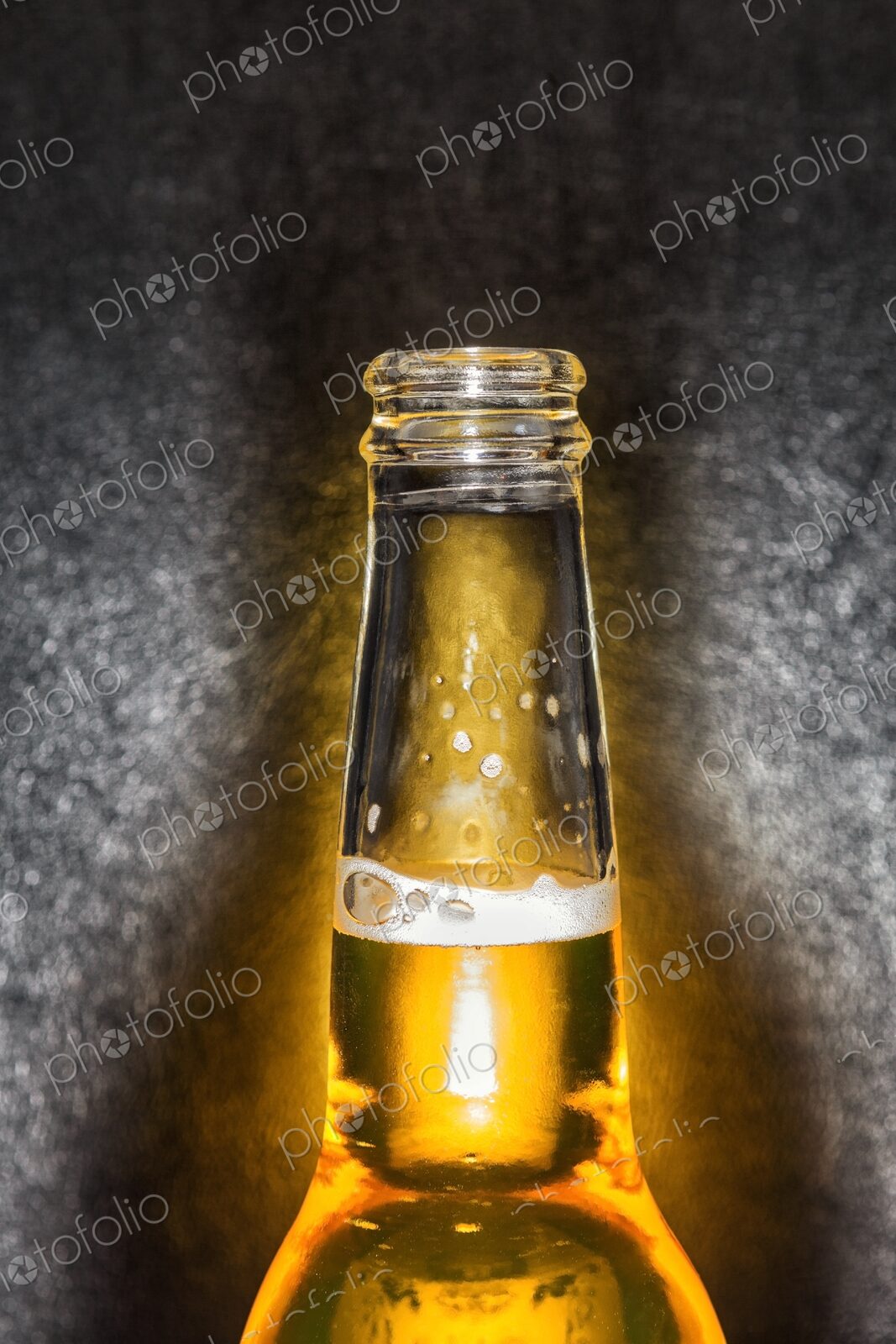 Closeup of clear glass beer bottle with cold beer against a black leather background