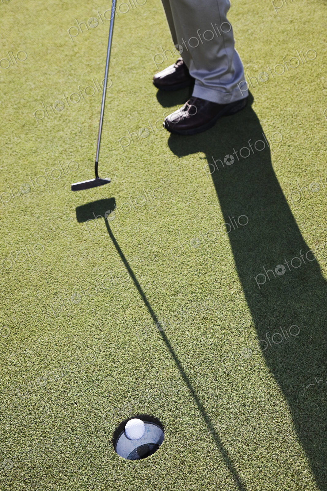 Closeup of golfer hitting a put and a golf ball going into the cup