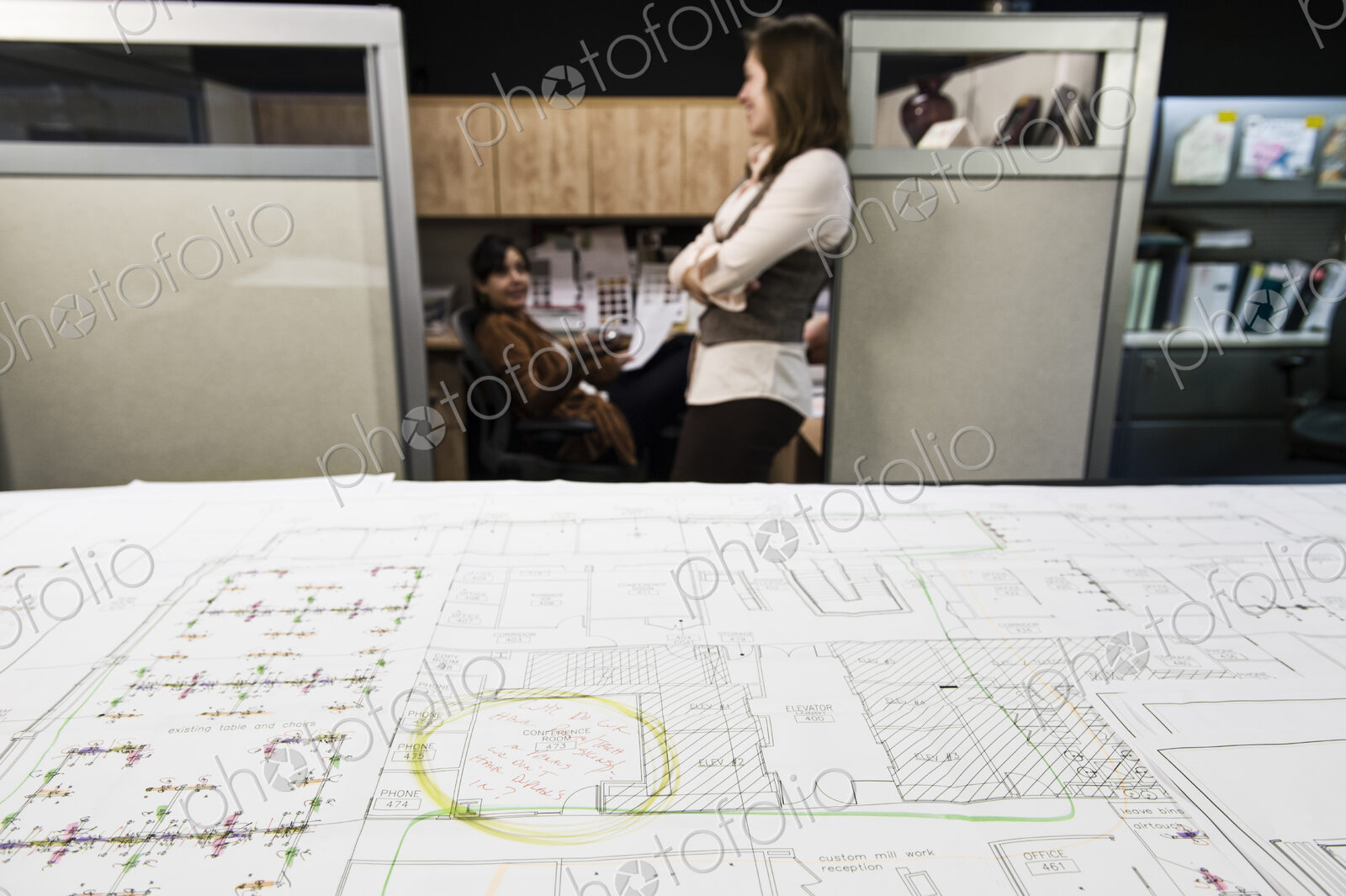 Closeup of plans on a table with two people working in the background.