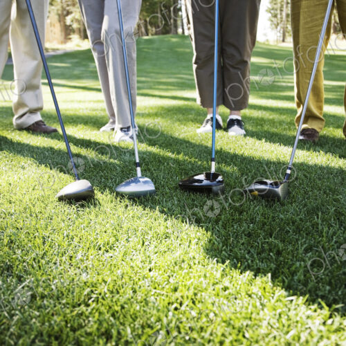 Closeup of the feet of four golfers and the head of their driver clubs.