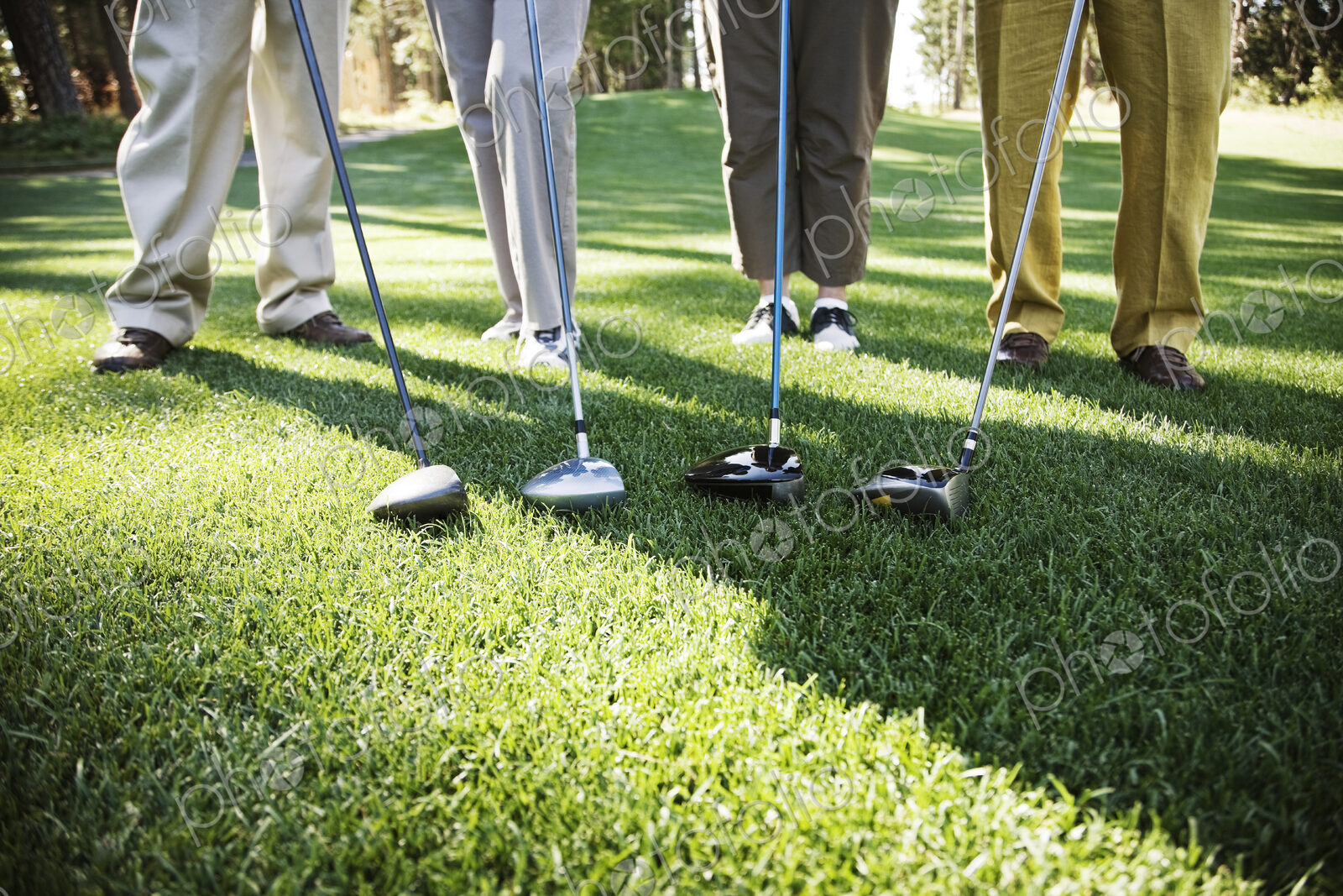 Closeup of the feet of four golfers and the head of their driver clubs.