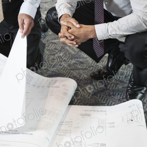 Closeup of two men going over plans for a new office space while kneeling on an office…