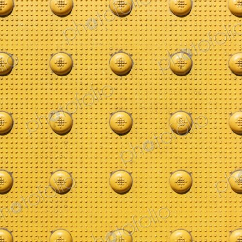 Closeup of yellow bumps on sidewalk near corner of an intersection. Officially called…