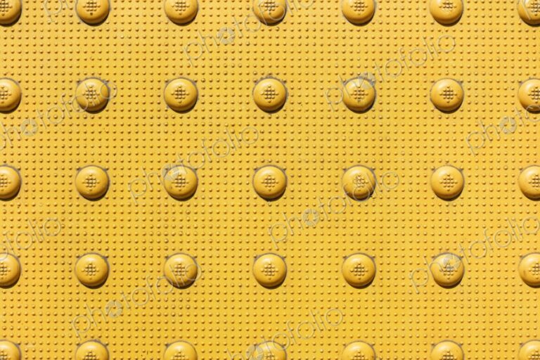 Closeup of yellow bumps on sidewalk near corner of an intersection. Officially called…