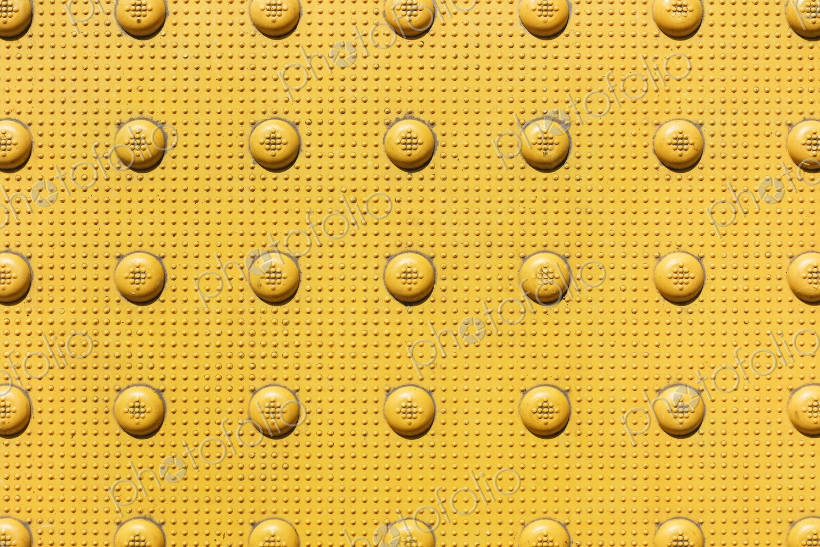 Closeup of yellow bumps on sidewalk near corner of an intersection. Officially called…