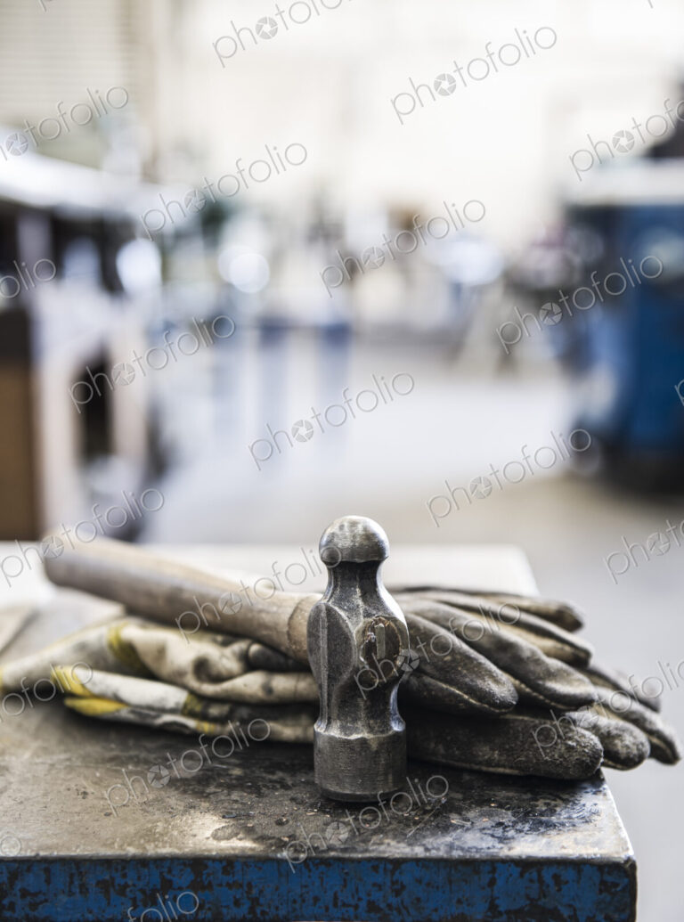 Closeup still life of gloves and a heavy duty hammer in a sheet metal factory.