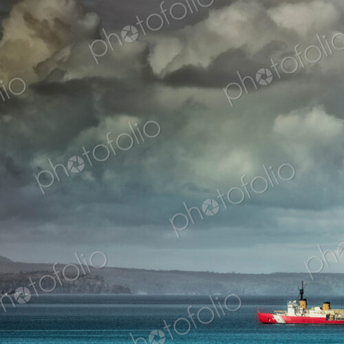 Coastguard boat sailing along coastline under moody sky.
