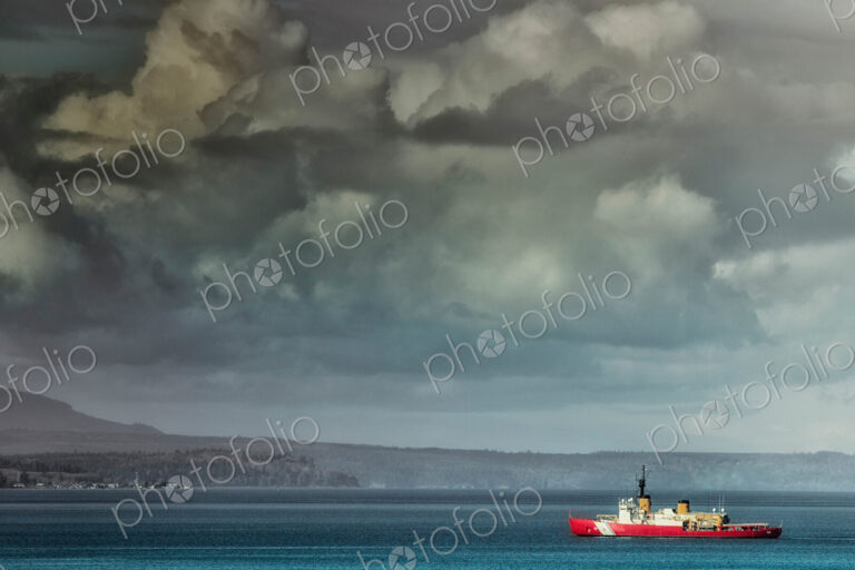Coastguard boat sailing along coastline under moody sky.