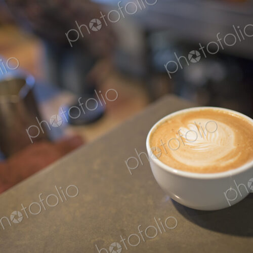 Coffee shop table. A full white china cup of coffee with a frothed milk top.