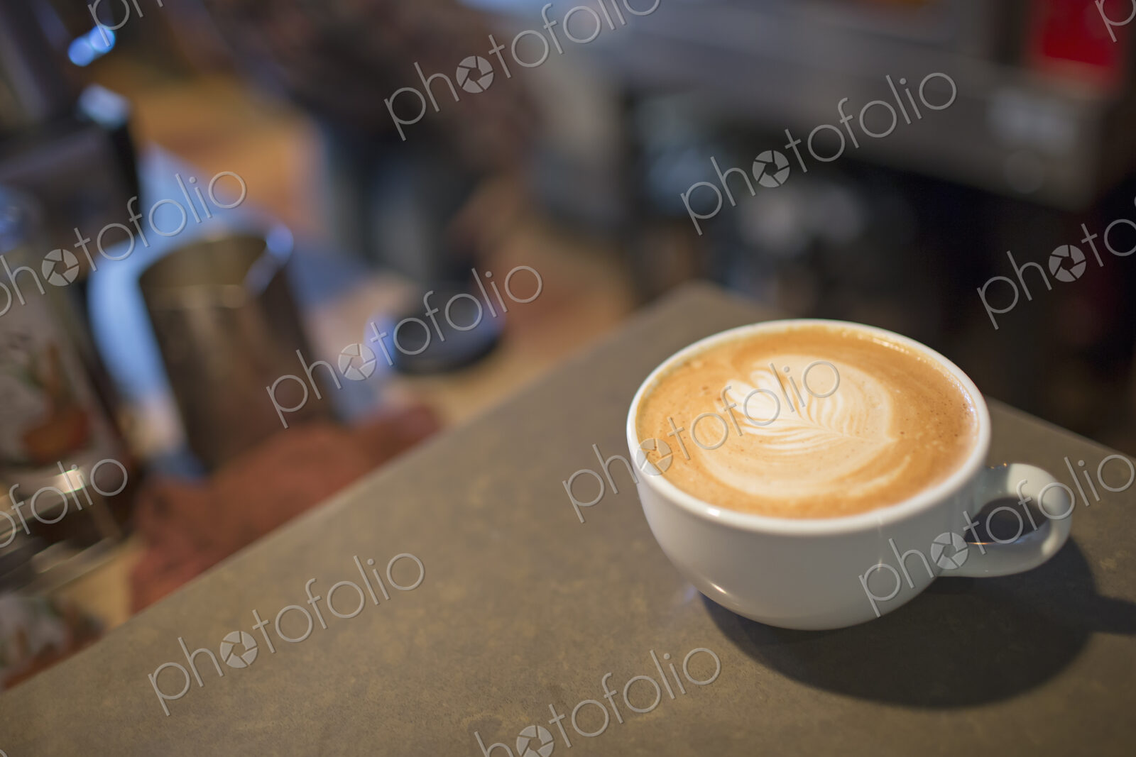 Coffee shop table. A full white china cup of coffee with a frothed milk top.