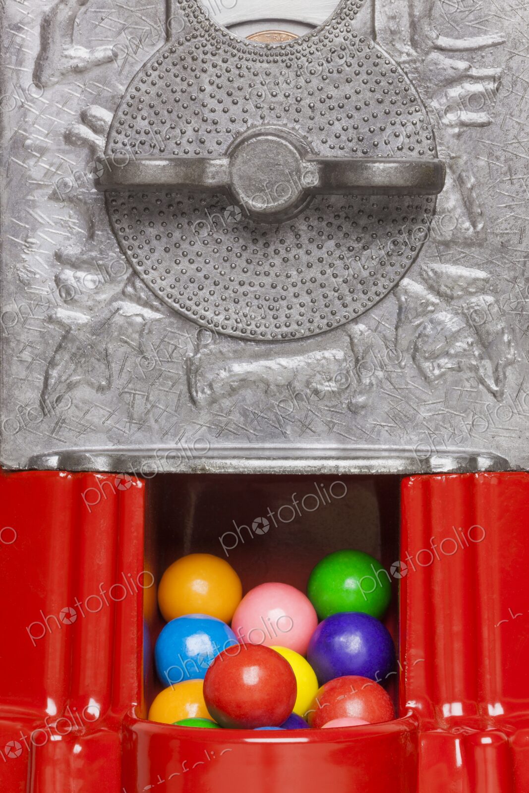 Colorful gumballs visible inside the dispensing slot of a red vintage gumball machine…