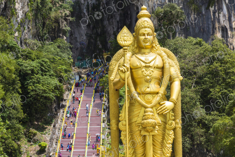 Colossal golden statue of Hindu deity, with stairway into cave in the background.
