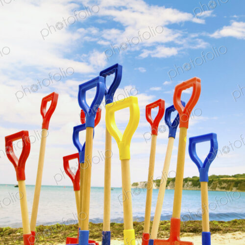 Colourful childrens' spades stuck in sand on beach.