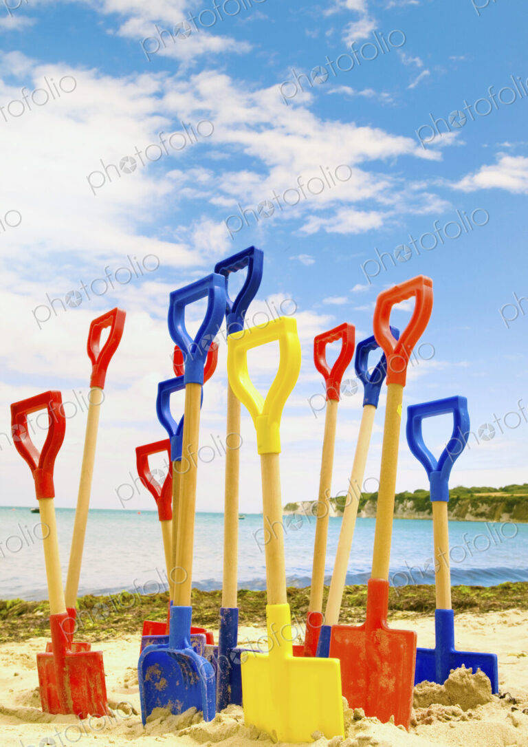 Colourful childrens' spades stuck in sand on beach.