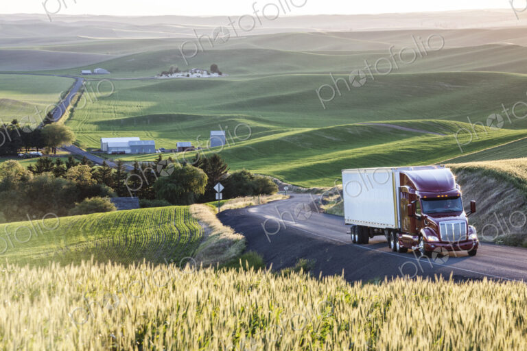 Commercial truck driving though wheat fields of eastern Washington, USA at sunset.