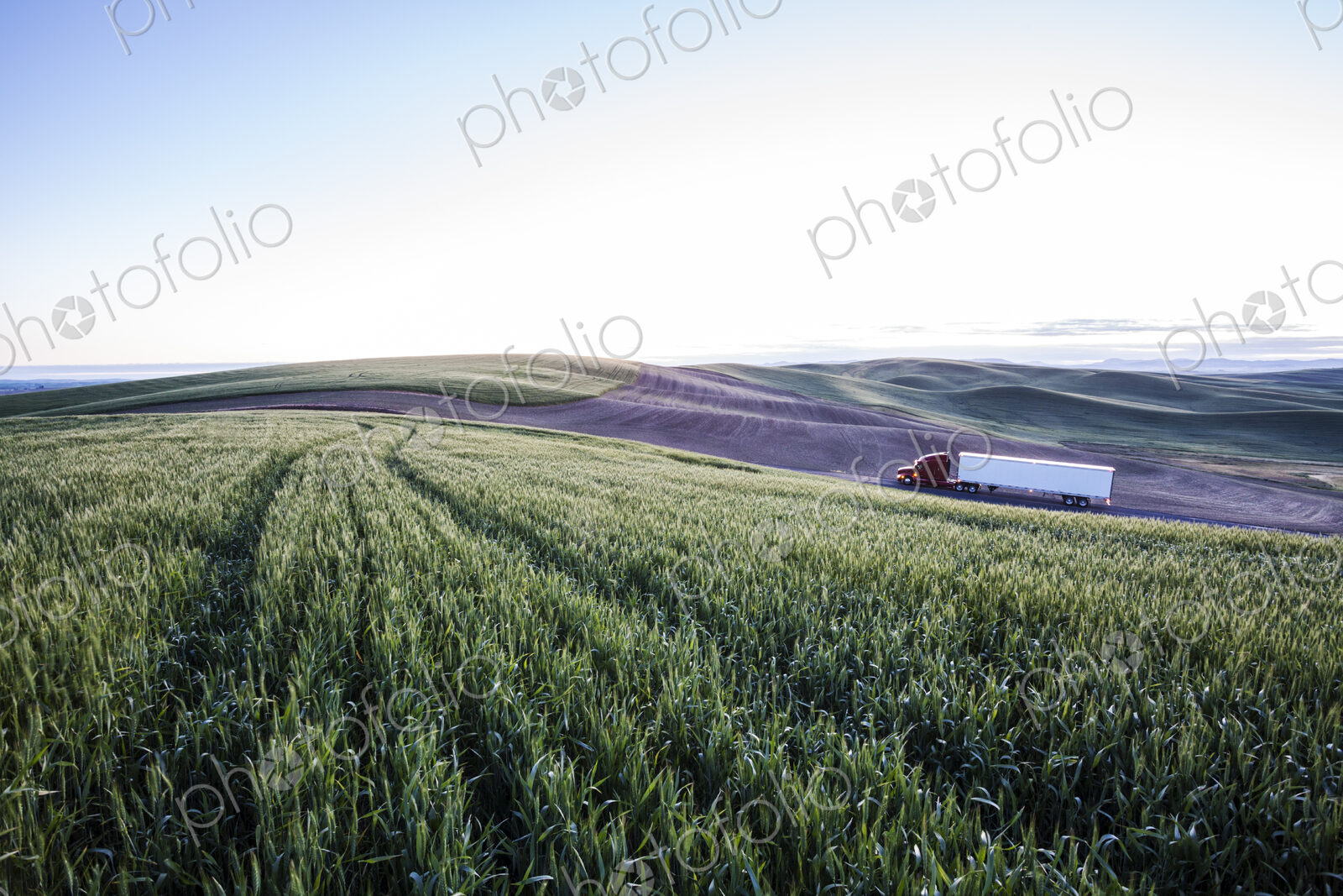 Commercial truck driving though wheat fields of eastern Washington, USA at sunset.